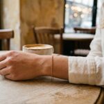 Femme portant un bracelet fin en or sur un poignet posé sur une table de café parisien