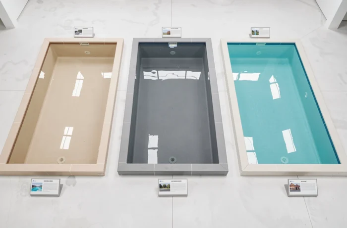 Vue aérienne de trois sections de piscine en showroom avec des liners de couleurs différentes — beige sable, gris ardoise et turquoise — pour comparer l'effet sur la teinte de l'eau
